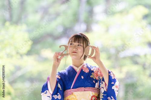 A local city in Japan on a rainy summer day. A Japanese woman wearing a blue teenage kimono in a traditional garden. She holds blocks of 2 and 0 in her hand and laughs. Celebration of 20 years old.