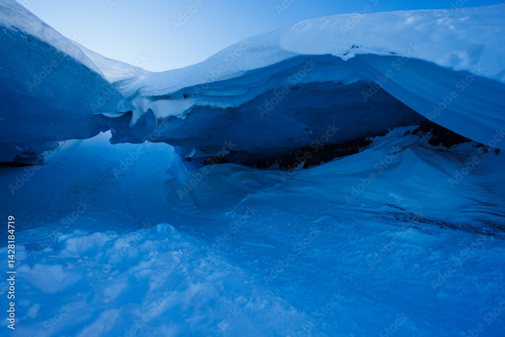 Blue ice glacier cave entrance under vast snowy cover at dusk
