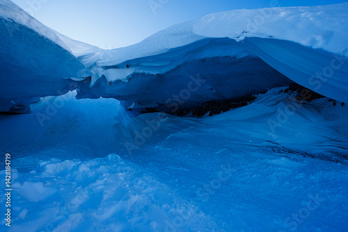 Blue ice glacier cave entrance under vast snowy cover at dusk