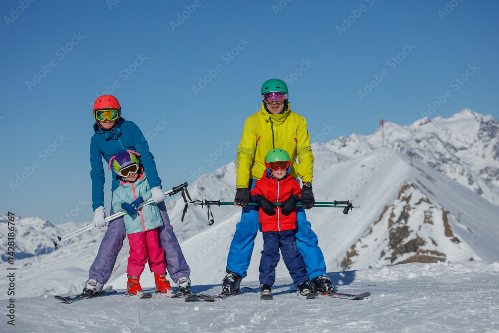 Happy parents with kids ski in snowy mountains under blue skies