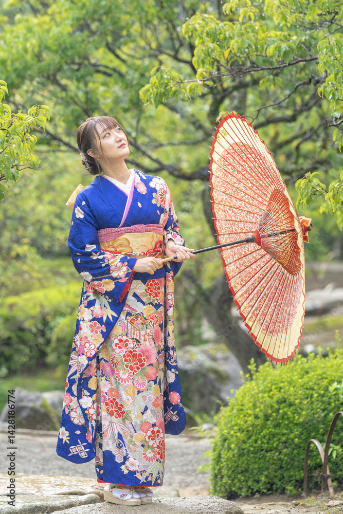 A local city in Japan on a rainy summer day. A Japanese woman wearing a blue teenage kimono with a Japanese umbrella in a traditional garden.