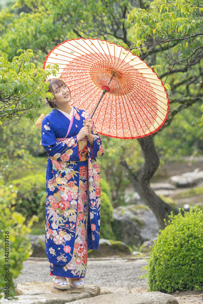 A local city in Japan on a rainy summer day. A Japanese woman wearing a blue teenage kimono with a Japanese umbrella in a traditional garden.