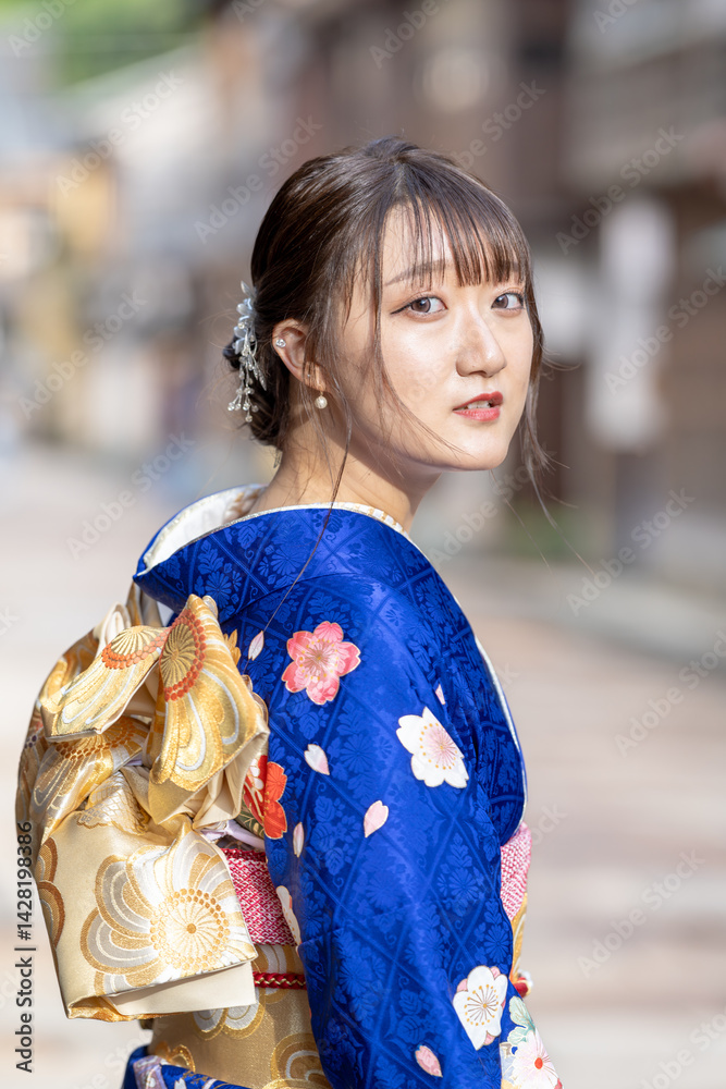 A teenage Japanese girl wearing a blue kimono standing in a view of traditional towns in a local city in a rainy summer day. She's turning around.
