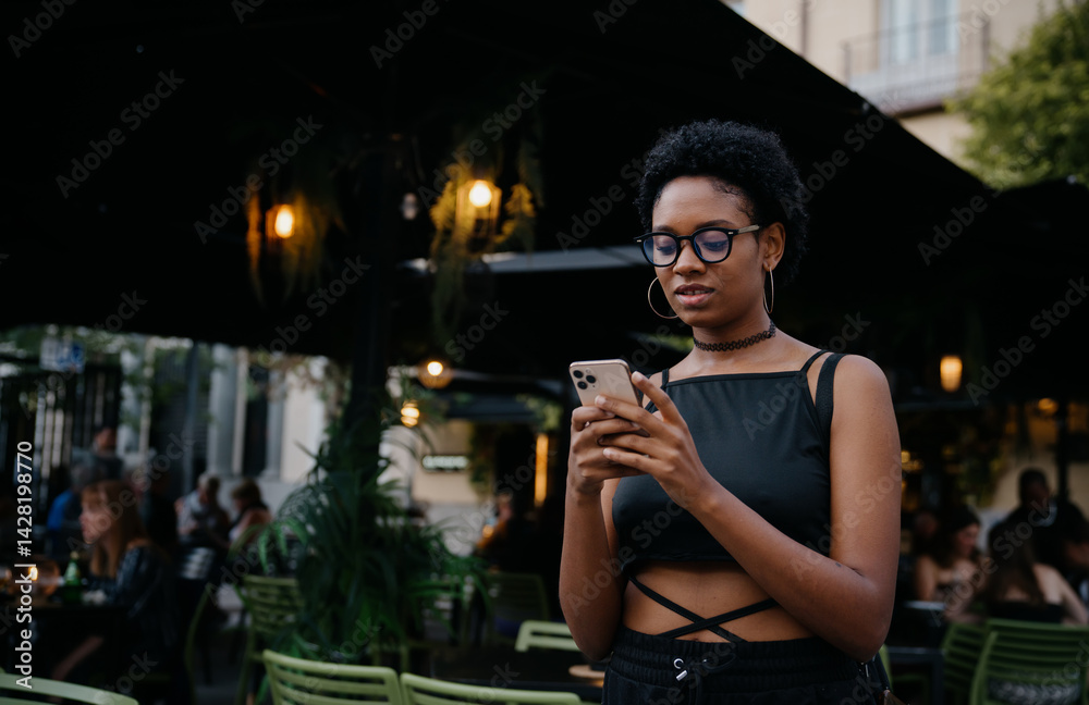 Trendy woman holding smartphone while checking messages in outdoor evening café, blending technology with relaxed ambiance and modern lifestyle in urban nightlife scene