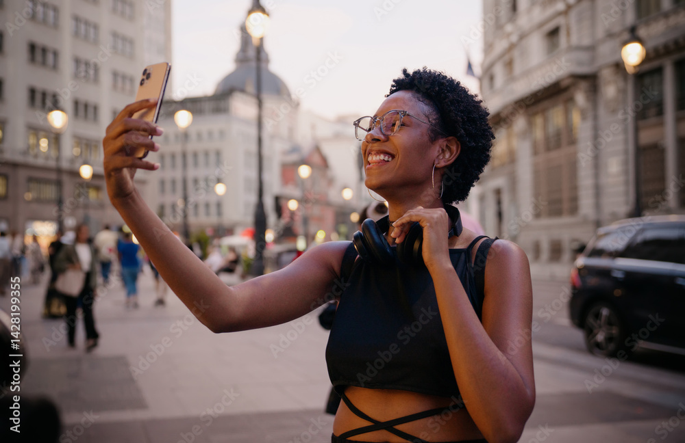 Happy young Black woman enjoying video chat while traveling in Europe, city lights glowing behind her, sharing real-time connection with followers or family
