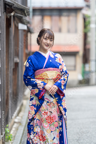 Obraz na płótnie A teenage Japanese girl wearing a blue kimono stands in the landscape of a traditional town in a Japanese city on a rainy summer day. She stands by a wooden building. w salonie