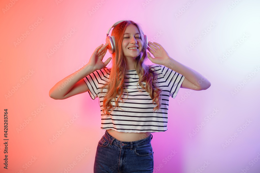Young woman enjoying music with headphones while posing against a colorful background in a studio setting