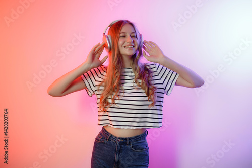 Obraz na płótnie Young woman enjoying music with headphones while posing against a colorful background in a studio setting w salonie