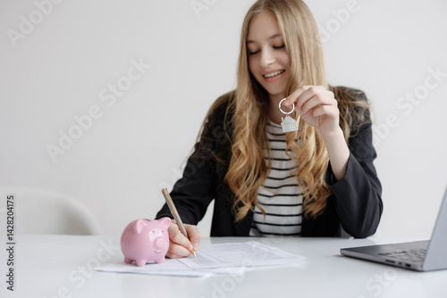 Obraz na płótnie Young woman completing paperwork for new home purchase while holding house key and sitting next to piggy bank w salonie