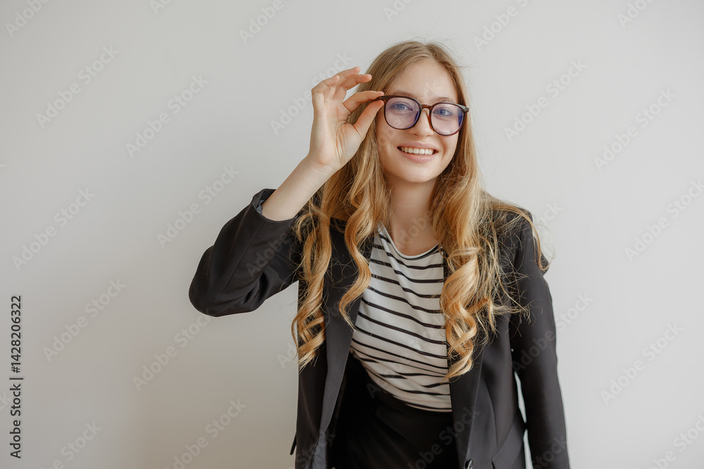Young woman with long hair wearing glasses and a striped shirt poses confidently in a black blazer indoors