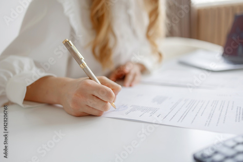 Obraz na płótnie Woman writing on documents at a white desk with a calculator and office supplies in a well-lit workspace w salonie