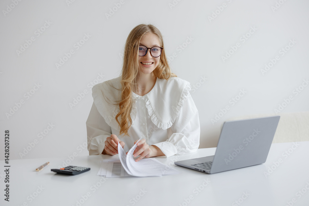Young woman reviews paperwork while working at a minimalistic desk during daylight hours
