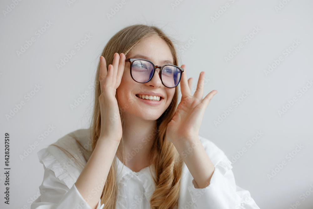 Young woman with glasses smiling and adjusting her glasses in a bright indoor setting