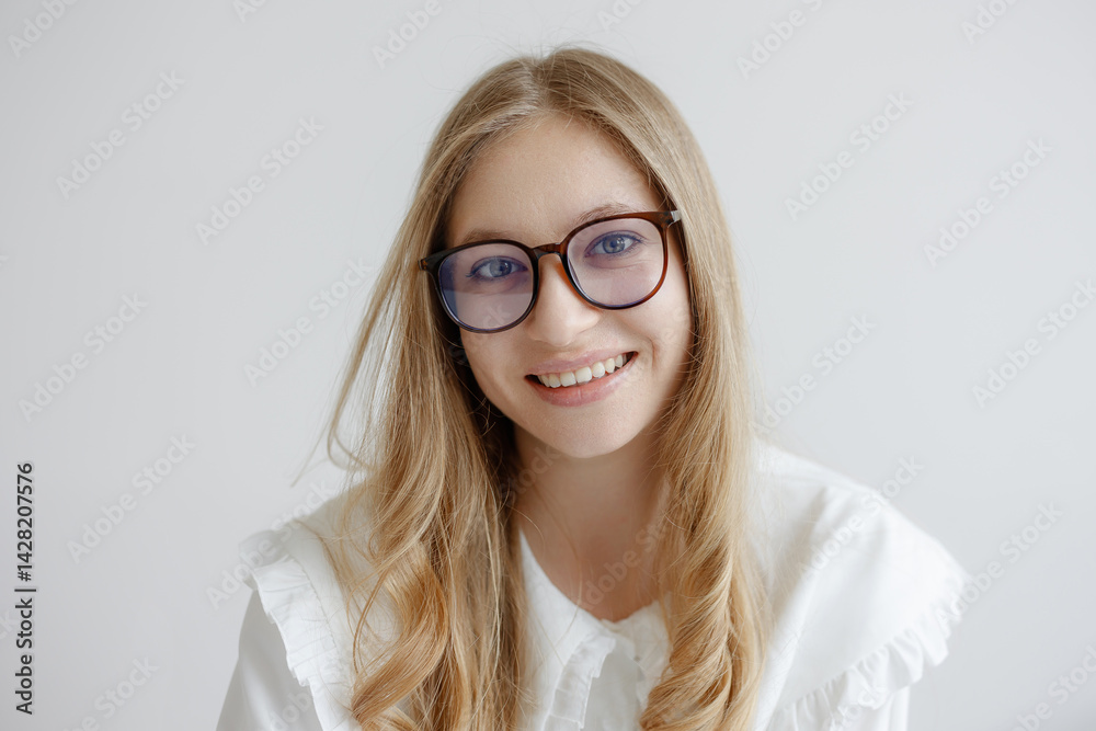 Young woman with glasses smiles warmly while sitting against a light background in a bright indoor space