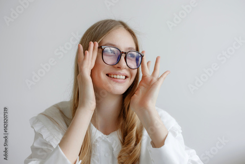 Obraz na płótnie Young woman with glasses smiling and adjusting her glasses in a bright indoor setting w salonie