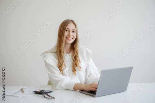 Obraz na płótnie Young woman working on a laptop in a bright, minimal office while smiling towards the camera w salonie