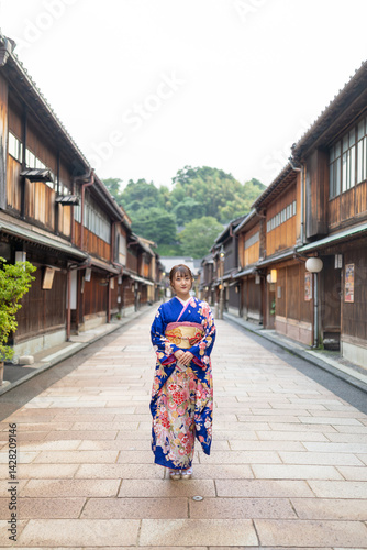 Obraz na płótnie A teenage Japanese girl wearing a blue kimono stands in the view of a traditional town in a local Japanese city on a rainy summer day. w salonie