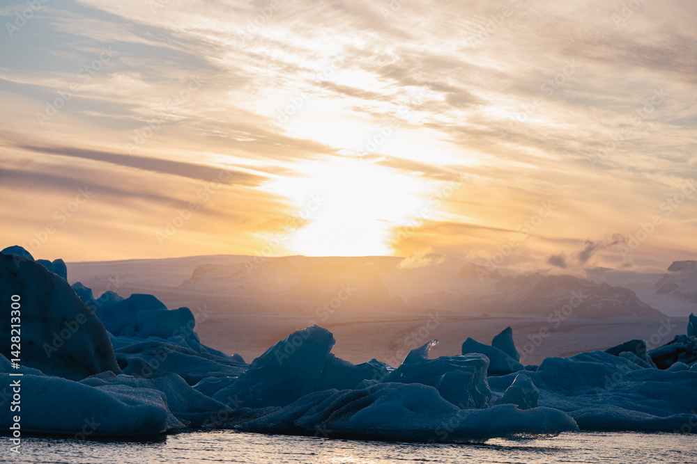 A breathtaking view of melting icebergs at Jökulsárlón as the sun sets behind the glacier, casting soft light on the arctic seascape.