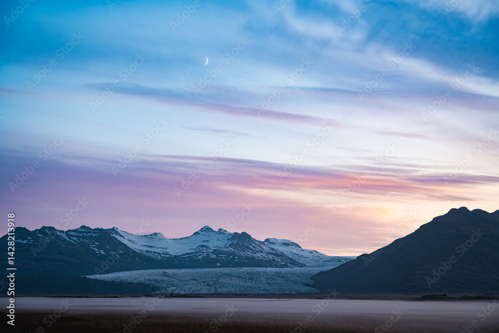 Twilight over Vatnajökull glacier in Iceland, with snow-covered peaks, pastel sky, rising crescent moon, and mist-covered plains evoking stillness and grandeur.