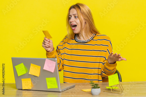 Exhausted woman sitting at table with pasted sticker notes use laptop computer having concentration problem creative crisis. Nervous girl confused by big routine work loading on yellow background