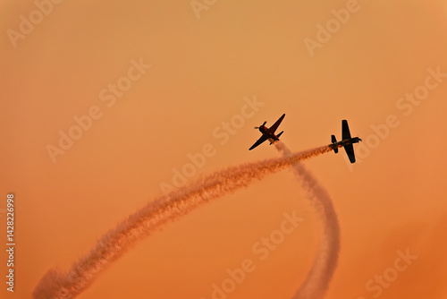 two planes synchronously flying during an aerial performance on the beatiful sunset orange sky