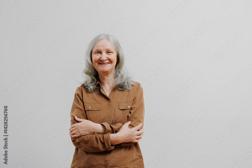Elderly woman smiling with crossed arms in a simple indoor setting during daylight hours