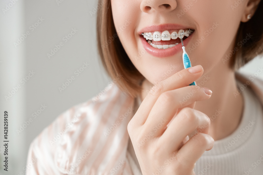 Young woman with dental braces cleaning teeth in bathroom, closeup