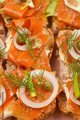 An assortment of open-faced sandwiches featuring carrot slices prepared as vegan salmon, arranged in a clear container