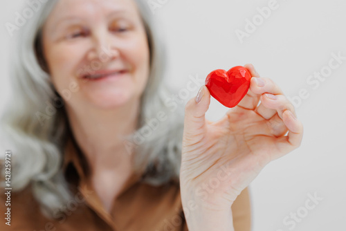 Wallpaper Mural Senior woman holding a red heart-shaped object, expressing joy and affection in a bright, minimalistic setting Torontodigital.ca