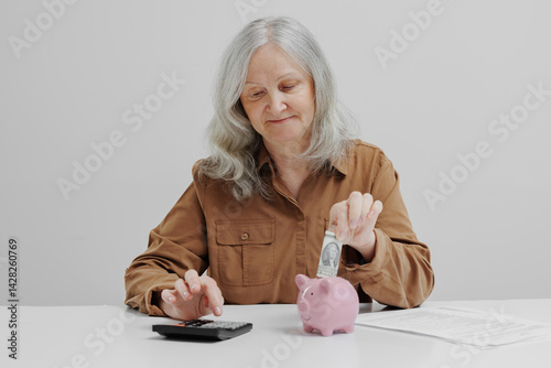 Obraz na płótnie Elderly woman saving money in piggy bank while using calculator for budgeting in a minimalistic environment w salonie