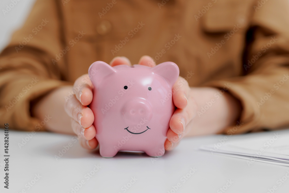 Holding a pink piggy bank while planning savings for future financial goals in a bright workspace