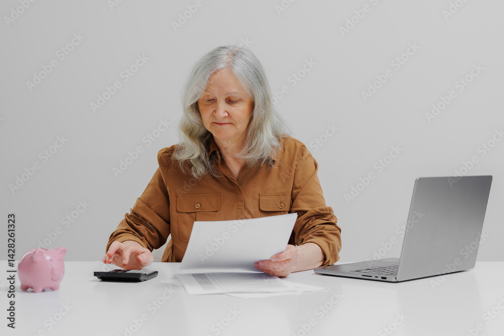 Senior woman managing finances with calculator and documents during daylight