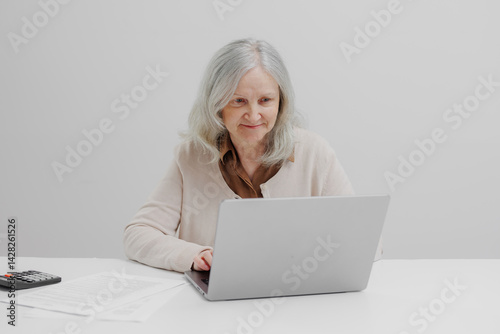 Obraz na płótnie Senior woman using laptop while sitting at a desk with documents and a calculator in a modern office environment w salonie