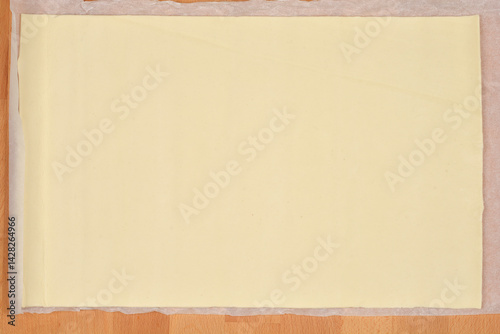 Obraz na płótnie A sheet of store-bought pale yellow puff pastry sits unfolded on parchment paper atop a wooden surface w salonie