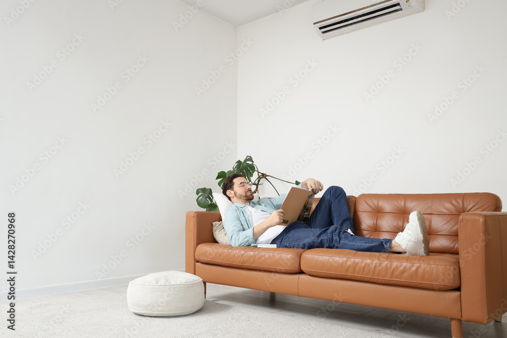 Handsome man reading magazine with air conditioner in living room Handsome man reading magazine with air conditioner in living room