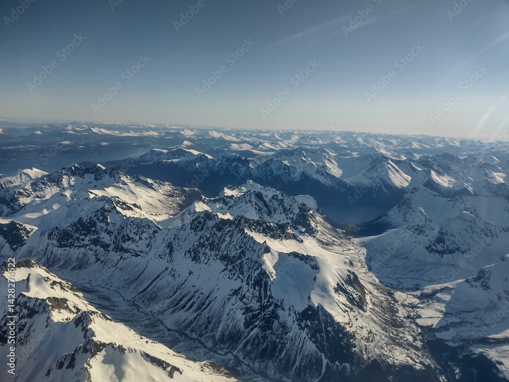 Fototapeta premium Aerial view of snow-covered mountains under a clear sky.