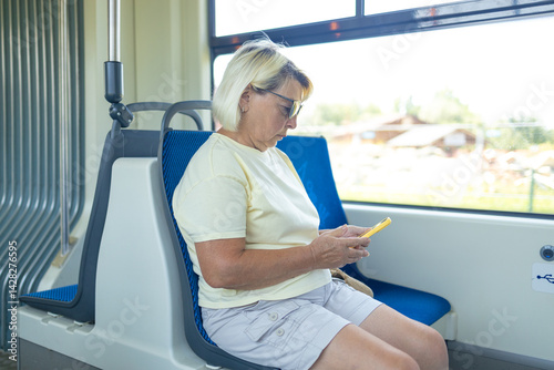 Obraz na płótnie Old European woman sitting in streetcar and using smartphone while waiting for next stop and going home. High quality photo w salonie