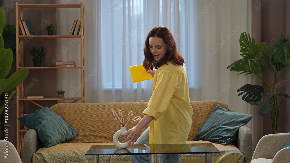 Young adult woman spending time at home, housekeeping time on weekend, woman in the living room cleaning wiping the dust from the glass table. Young adult woman spending time at home, housekeeping time on weekend, woman in the living room cleaning wiping the dust from the glass table.