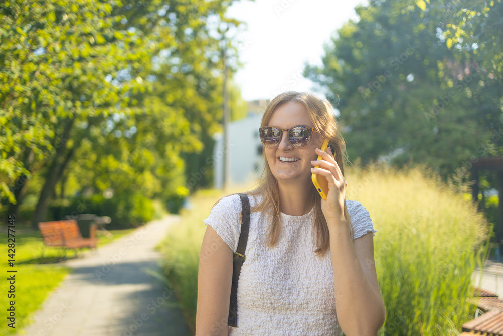 Portrait of smiling 30s student freelancer woman looking at the camera talking on phone in summer park. People urban lifestyle concept. High quality photo