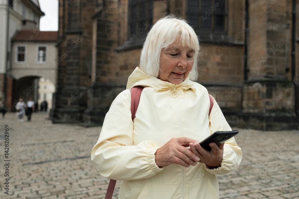 Caucasian senior 50s 60s woman holding backpack on shoulder sightseeing in old town of Praha, looking at map in a smartphone enjoying travel tourism and freedom.