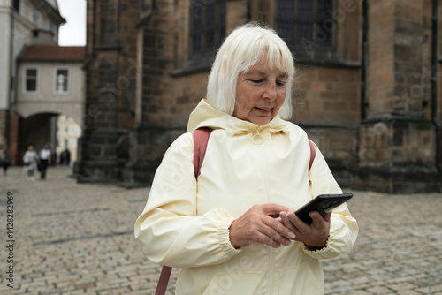 Obraz na płótnie Caucasian senior 50s 60s woman holding backpack on shoulder sightseeing in old town of Praha, looking at map in a smartphone enjoying travel tourism and freedom. w salonie