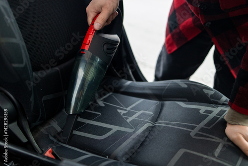 Details of car vacuum cleaning. Professional cropped male worker using wet vacuum cleaner for dirty car interior. Auto car service cleaning the drivers seat, cleaning and vacuuming concept. High