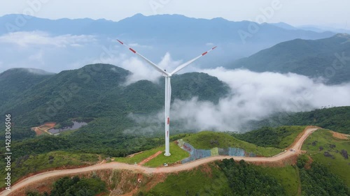 Cloudy aerial view of wind turbine surrounded by mountains and mist in serene landscape