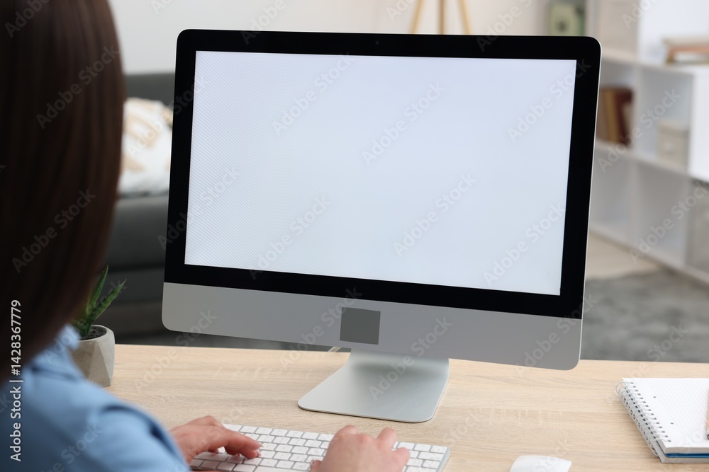 Woman looking at monitor with blank screen at wooden table indoors. Mockup for design