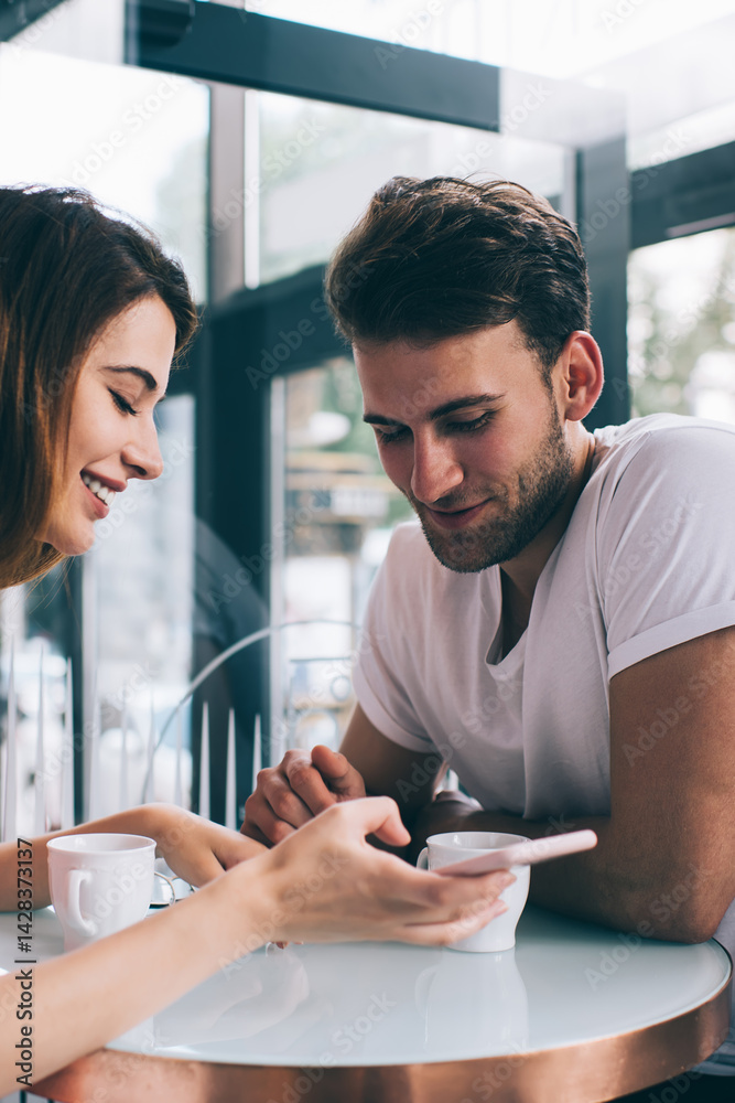 Happy couple using smartphone while sitting in cafe in daytime