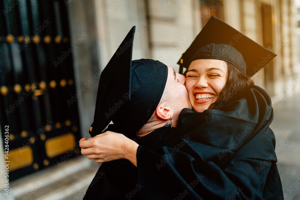 Two happy students are hugging and celebrating their graduation day in front of their university