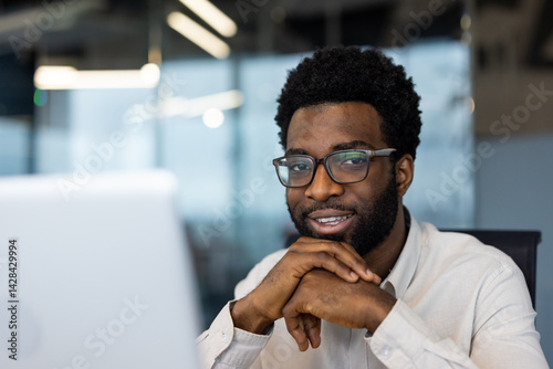 Obraz na płótnie A professional man smiles warmly, looking directly at the camera. He wears glasses and is at his desk, ready for work. w salonie