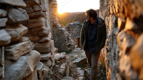 Young Man Walking Through Historic Stone Village Ruins at Sunset with Autumn Foliage in Background photo