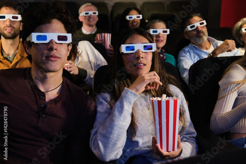 Obraz na płótnie Group of young people wearing 3d glasses watching a movie at the cinema and eating popcorn w salonie