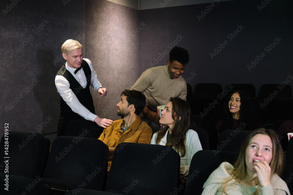 Movie theater employee guiding people to their assigned seats while other spectators are already watching the film